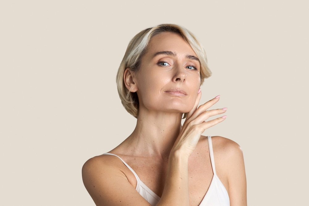 Woman wearing a white top touching her face gently pleased with her aesthetic treatment done at Aesthetic Solace.