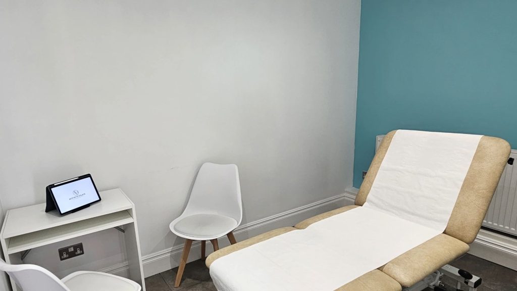 Aesthetic Solace calm and welcoming consultation room including a comfy treatment couch and a desk with chairs.